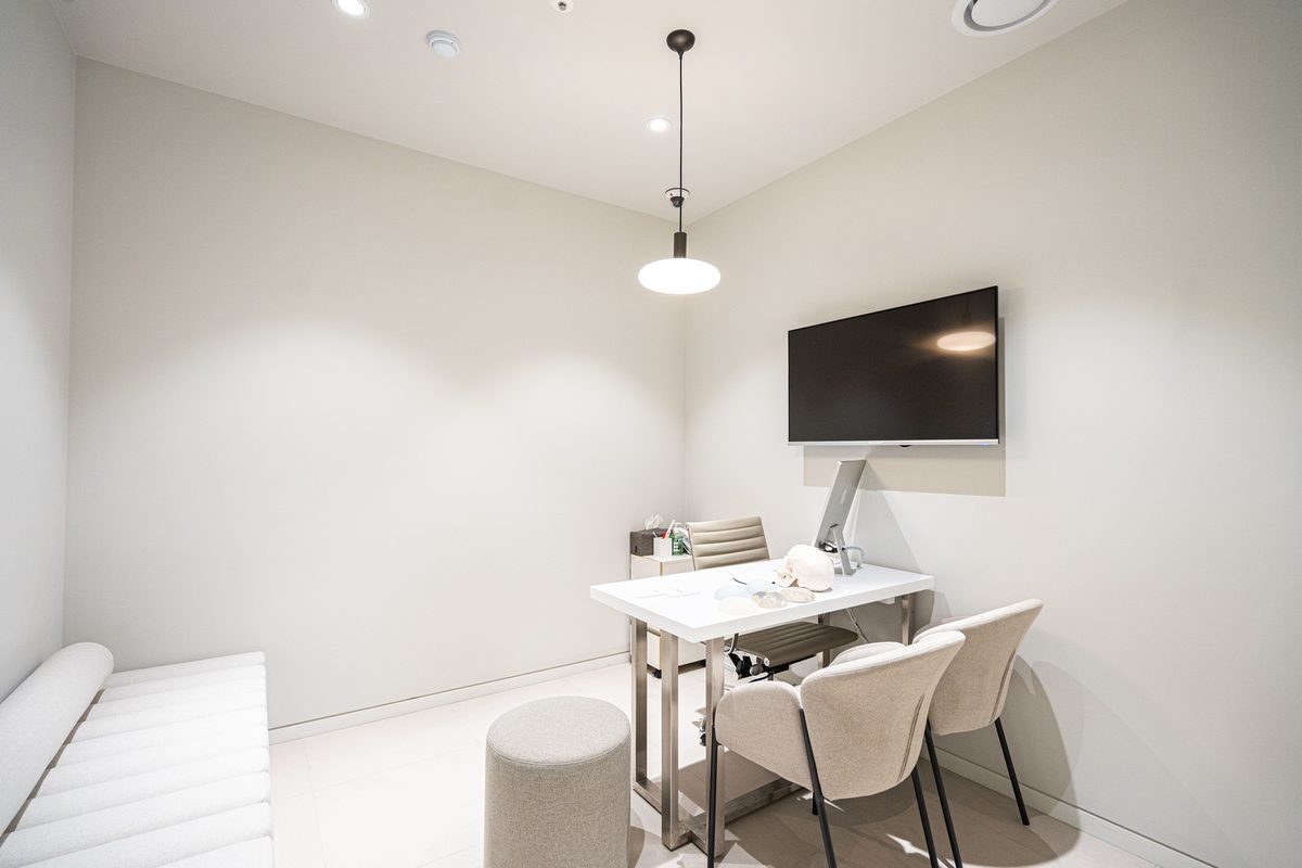 Consultation room with a pendant light, wall-mounted screen, and a desk holding breast implant sizers