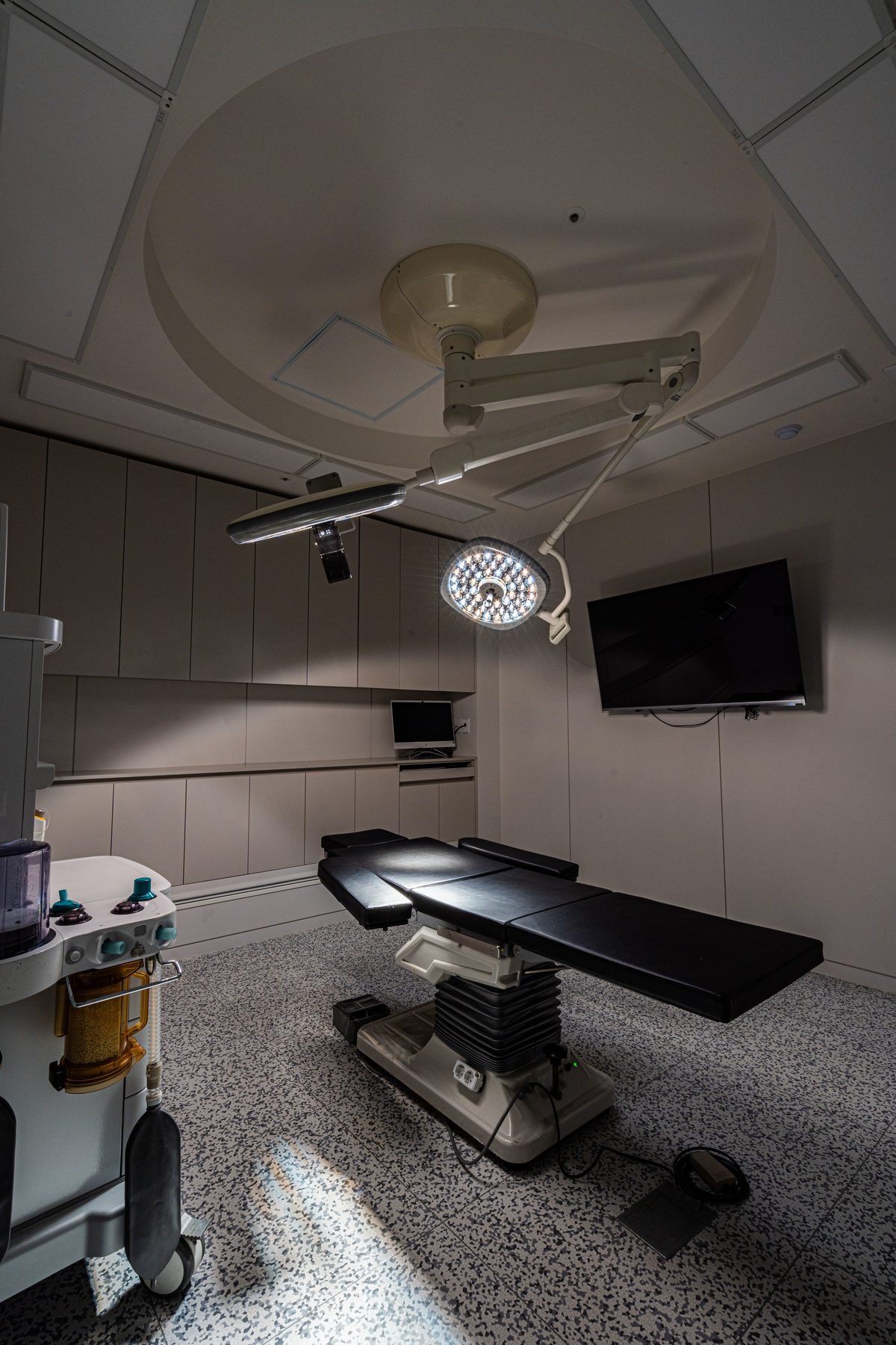 Operating room with dual surgical lights, a wall monitor, and an anesthesia machine